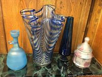 Four distinct blue glass pieces grouped on a shelf with a wooden back and marble surface.