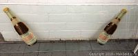 Two vintage Pepsi Cola glass bottles standing next to a white brick wall viewed from a distance.