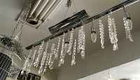 Linear chrome chandelier view showing hanging acrylic drops varying in shapes and sizes from a side angle.