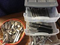 Photo of assorted silver plate and stainless forks, spoons, and knives in a woven basket and plastic bin drawers.