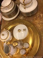 Overall view showing multiple cups, saucers, plates, and lidded containers arranged on a large gold-colored serving tray or charger.
