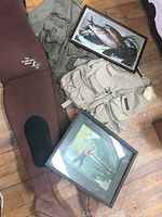 Overview photo showing two fishing vests, brown waders, and two vintage framed fishing prints on a wooden floor.