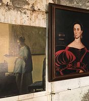 Two framed female portrait prints hanging on a wall; one woman in a blue dress reading, the other in a red dress with puffed sleeves.