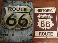 Two Route 66 metal signs displayed on a flat surface, showing both designs in full.