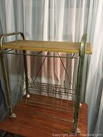 Full view of the vintage record rack showing wooden top shelf, metal frame with distressed patina, and wire record dividers on wheels.