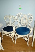 Front view of the King and Queen size white wicker chairs with blue cushions placed side by side on wood floor.