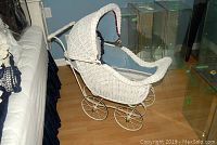 Full view of white wicker doll pram with curved hood and fabric lining in a room