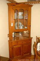 Full view of pine corner china cabinet showing glass door, mirrored back, drawer, and lower wood doors with natural finish.
