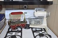 Kitchen stove with Great American Popcorn Machine and Sunbeam Mixmaster mixer with bowl and beaters placed on top.