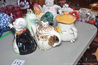 Photo displaying several ceramic teapots including owl and penguin designs arranged on a table