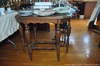 Full front view of wooden occasional table showing turned legs, carved apron, and stretcher supports.