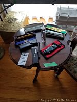 Photo of wooden side table with vintage straight razor, folding knife, various harmonicas and an illuminated microscope case.