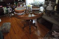 Round oak wooden table with pedestal base on caster wheels holding several decorative items including framed art and flower figurines.