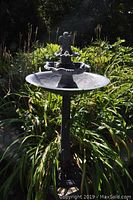 Full view of the metal bird bath standing in a garden surrounded by greenery and plants.
