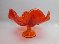Side view of orange glass bowl showing wavy rim and pedestal base