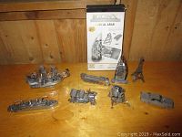 Several miniature metal 3D models arranged on a wooden table including ships, cars, a train, Eiffel Tower, and Burj Al Arab.