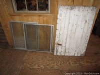 Photo showing white wooden door with peeling paint and six aluminum framed windows leaning against a wooden wall.