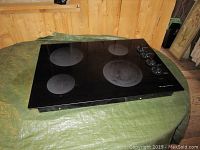 Frigidaire electric range top placed on a green tarp against a wooden background, showing the four burners and overall surface condition.