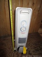 Frontal view of the white Honeywell oil-filled radiator heater showing control knobs and height with measuring tape.