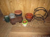 Shows all garden pots, watering can, and metal flower pot stand grouped together on wooden floor