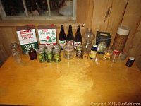Lot of vintage bottles, cans, and containers on a wooden surface inside a rustic room, showing variety of collectible items.