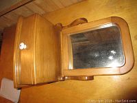Wooden wall shelf with a drawer and swivel mirror viewed from above. Shows the curved shape of the mirror frame and white knob drawer.