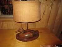Full view of the wooden duck lamp with beige fabric shade on a wooden surface, showing overall size and condition.