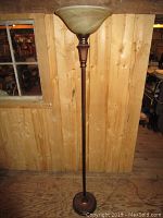 Full view of the floor lamp showing the bronze-colored base, pole and green marbled glass shade, standing against a wooden wall.