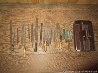Large assortment of hand files and rasps on a wood surface including a brown metal toolbox.