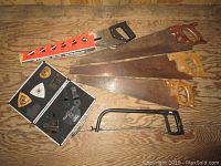 Photo showing four wood hand saws with wooden handles, hacksaw, and metal framed blades laid on a wood surface