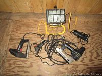 Photo of work light, power staplers, heat gun and glue gun on wooden floor, showing all 5 items with cords tangled