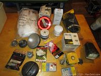 Wide shot showing all parts spread on table including filters, gas caps, wheel lock key, vehicle lights, spark plug cables, and packaging.