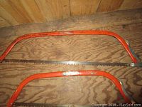 Two orange metal buck saws displayed on wooden floor. Larger with 30-inch blade, smaller with 24-inch blade.