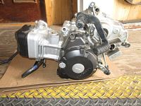 Side view of Honda 125cc motorcycle engine showcasing engine casing, black gear shift lever, and foot peg.