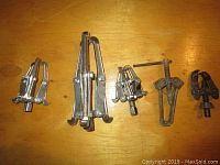 Five metal gear pullers of various sizes arranged on a wooden surface, showing all units from front view.