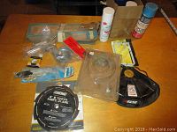 Overview of lot on table showing various items including spray cans, knife blade, weed wacker guard, shelf bracket, and small hardware