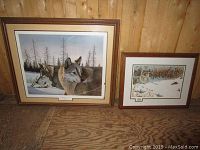 Two framed animal prints side by side on wood floor with wood wall background; left print with wolves, right print with rabbits