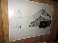 Framed print of a barn with a red tractor inside, hung on a wood-paneled wall.