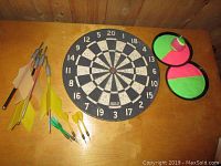 Photo showing all items in the lot: dart board, multiple darts, lawn darts, and velcro catch mitts with ball.