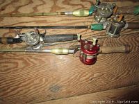 Four vintage fishing rods laid parallel on wooden floor, showing attached reels with various colored handles including green and yellowish plastic.