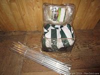 Green and white fabric tent packed in a clear plastic bag with label inside, placed on wooden floor