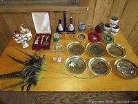 Full overview of lot items on wooden table including brass plates, frames, feathers, bottles, and figurines