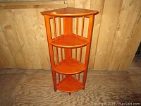 Wooden four-tier folding corner shelf standing unfolded showing front and side vertical slats supporting triangular shelves.