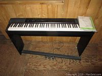 Full view of the Casio Privia digital keyboard on stand with foot pedals visible on the floor and instruction manuals on top.