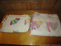 Two folded antique quilts on wooden surface showing colorful patchwork on white base fabric
