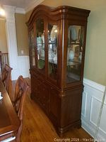 Right side angled view of the wooden china cabinet showing glass doors, storage drawers below, and polished wood finish.