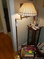 Full view of the gold-toned floor lamp with pleated fabric shade and adjustable arm near doorway and other furniture.