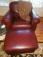 Front view of burgundy leather armchair with ottoman and textured throw blanket draped over chair back.