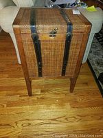 Front view showing wicker woven panels framed in wood, vertical leather straps, and metal latch lock.