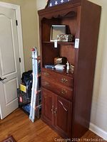 Front view of the wooden bookcase, showing open shelf with decor, two drawers, and cabinet doors below.